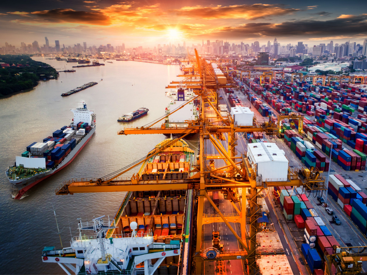 Photo of a shipyard with a crane, a ship, and lots of containers